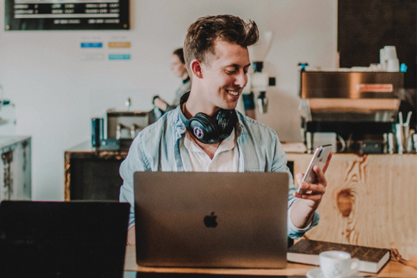 Guy using his phone and computer in a cafe