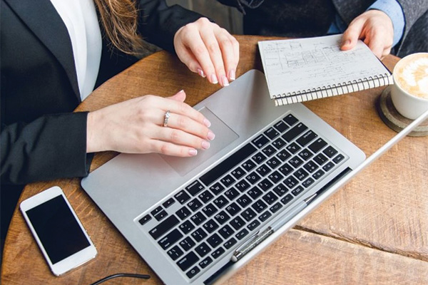 Two people using a computer and holding a notebook with only their hands showing